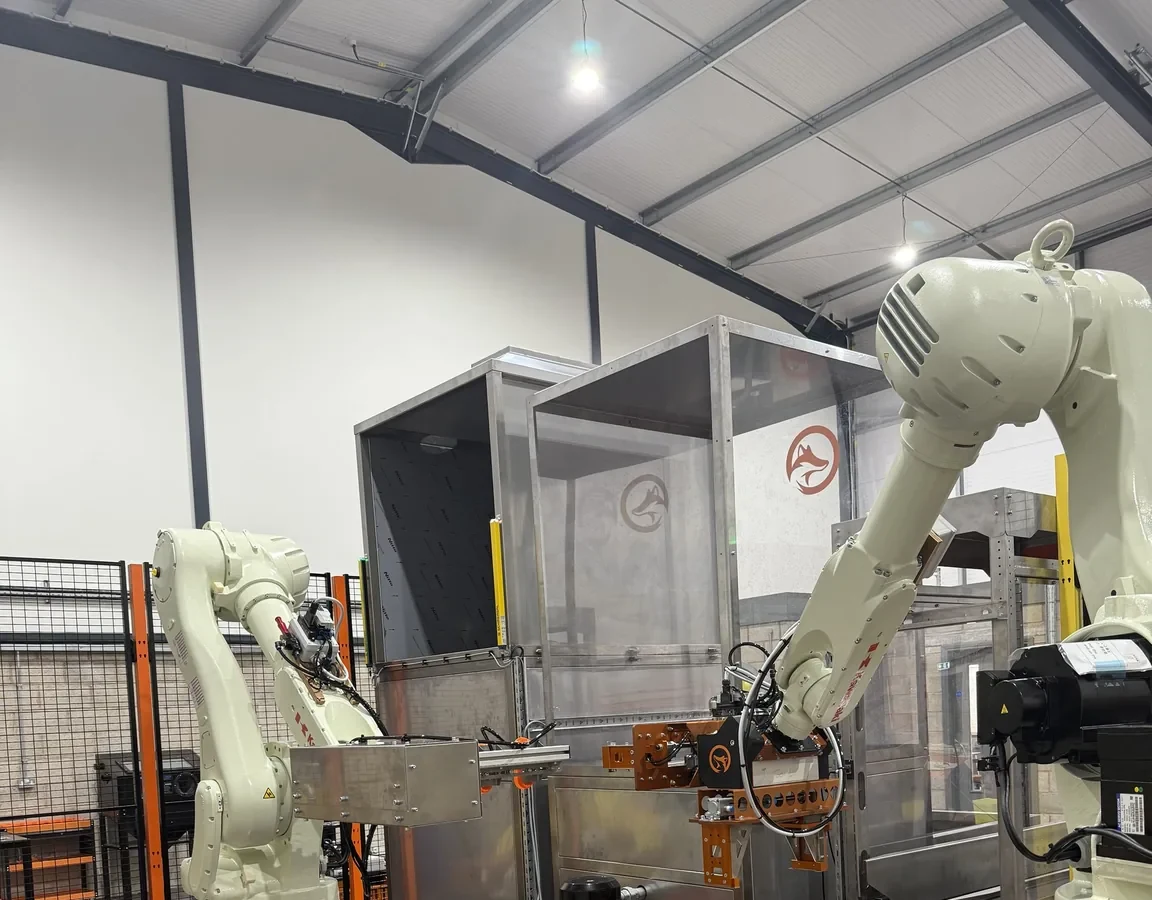 Two Fox Precision Tooling robots working together around a stainless steel enclosure