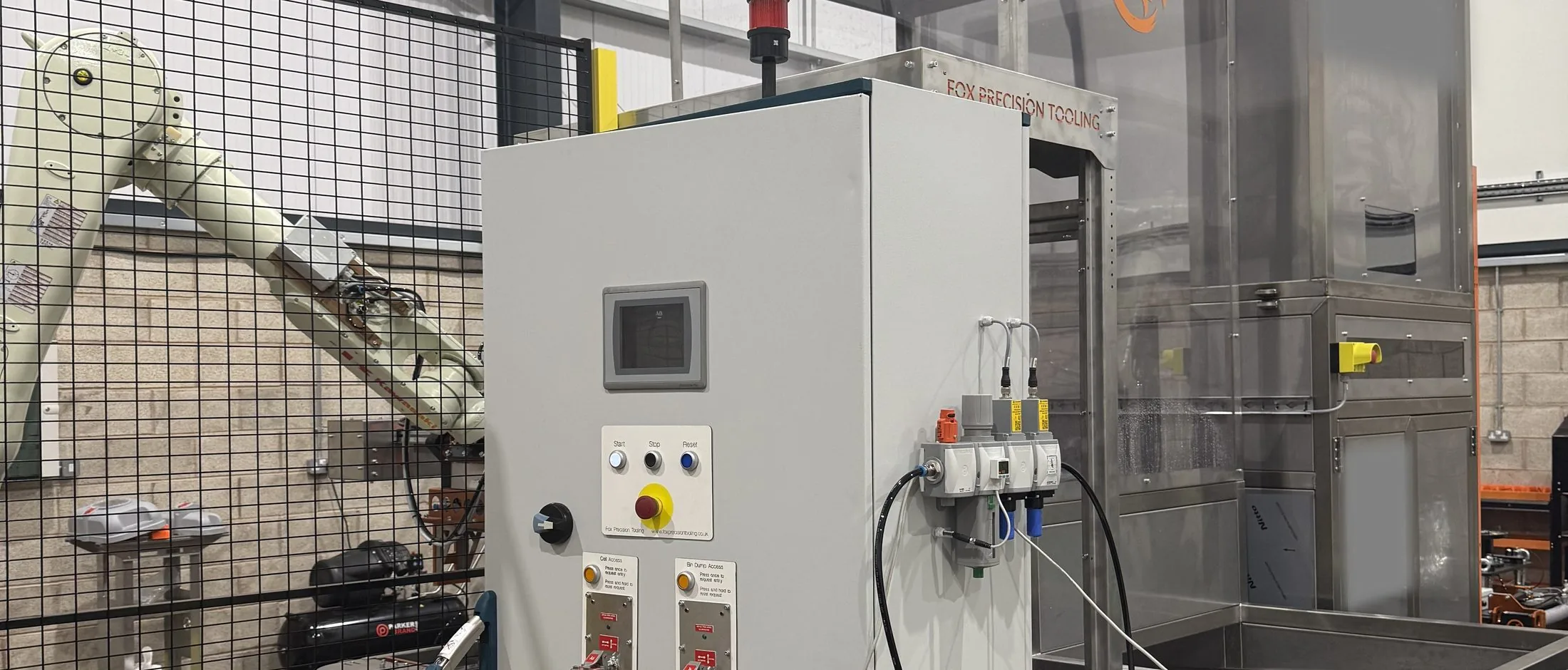 Fox Precision Tooling robot cell control cabinet and robot arm on the workshop floor, with the Stericycle-branded enclosure behind